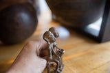 Hand holding a vintage African bronze figurine of two sitting figures, revealing its aged texture.