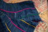 Close-up of vintage African indigo throw featuring vibrant pink, green, yellow embroidered details and frayed edge.