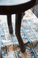 Vintage African wooden stool's dark brown, curved leg shows handcrafted wood texture.