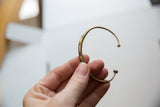 A vintage African bronze cuff bracelet held to show its delicate form and handmade markings.