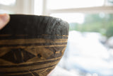 Dark wooden bowl with light carved geometric pattern, horizontal lines, and rim crack detail.