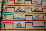 Handwoven straw construction of a vintage Tuareg mat showing colorful geometric thread patterns.