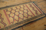 Vintage African Tuareg straw mat corner, displaying red and dark geometric patterns and fraying.