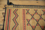 Vintage handwoven Tuareg mat, geometric red and black pattern on natural straw with frayed edge.