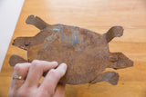 A hand holds the vintage African iron turtle, showing its weathered and rusted surface texture.