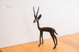 The slender body and textured, dark patina of a vintage gazelle figurine.