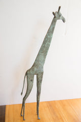 Vintage African giraffe figure standing, showing its slender form and oxidized patina.