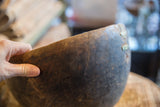 Hand holding vintage African wooden bowl with prominent crack and metal repair.