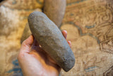 Antique African stone tool held to show its rounded shape and grainy texture.