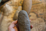 A hand holding an antique stone tool showing its rough, pitted surface texture.