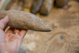 Hand holding the tapered point of a Neolithic stone weapon, showing its granular texture.