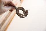 Hand holding the curved, double lizard pendant to show its scale and aged texture.