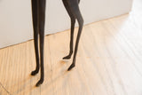 The slender, sculpted legs and small hooves of the dark giraffe figurine.