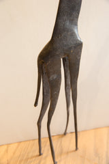 Rear view of the vintage African giraffe sculpture's slender legs, tail, and dark textured form.