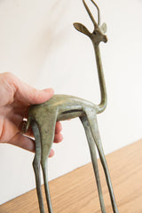 Hand holding the medium vintage African gazelle sculpture, highlighting its aged green patina.
