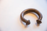 The curved form and dark, time-worn surface of an antique African copper cuff.