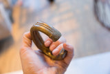 Antique bronze cuff held in hand, showing its substantial, curved form and texture.