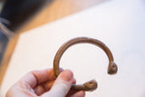 Hand-held view of an antique snake cuff's open design and etched copper surface.