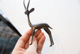 Vintage dark metal African gazelle figurine held in hand, showing aged patina.