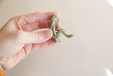 A hand holds the small bronze monkey figurine to show its scale and weathered texture.
