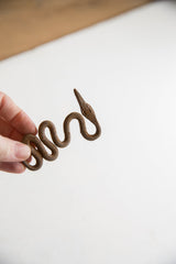 Vintage iron snake with a rustic patina held in hand for scale.