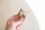Vintage bronze monkey figurine held in hand, displaying its side profile and ridged back.