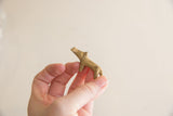 Vintage African brass mini hippo held in a hand to demonstrate its small size.