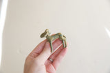 A hand holding the vintage impala ram gold weight, showing its small scale.