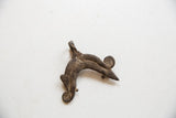 The sculptural form of a vintage African pendant with a dark, pitted surface and curled ends.