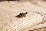 Profile view of a vintage bronze turtle pendant showing its detailed, open-work shell.