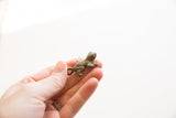 Side view of a vintage bronze frog pendant held to show its small scale and texture.