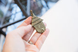 Vintage African bronze hut pendant held in hand, showing its scale and textured brick design.