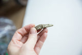 Side view of the small bronze crocodile pendant, held in hand to illustrate its size.