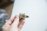 A hand holding the small bronze crocodile pendant to show its scale.
