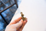 Profile view of the sitting monkey pendant showing its vintage brass texture.