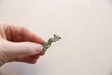 A small vintage bronze iguana pendant with an oxidized green patina held for scale.
