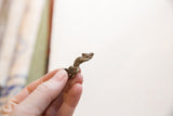 Vintage bronze iguana pendant held to show its small scale and aged patina.