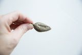 The three-dimensional form and incised details of the vintage bronze leaf pendant.