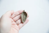 The textured reverse side of a vintage bronze leaf pendant with aged patina.