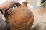 A hand holding the rustic clay handle of the antique North African vase.