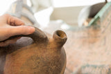 Close view of the antique vase's rustic, handmade handle and textured spout.