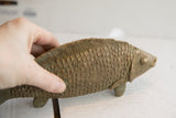 Hand holding vintage African fish sculpture, showing textured scales and green patina.