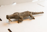 Full profile of a vintage African crocodile sculpture with hand-carved texture holding a fish.