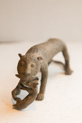The weathered, textured face of a vintage African cheetah sculpture holding prey.