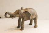 Vintage African elephant sculpture showing its weathered, handmade texture from a side angle.