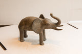 A vintage African elephant sculpture in profile with a rustic finish and raised trunk.