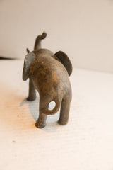 The back of the vintage elephant sculpture, showing its rustic texture and curled tail.