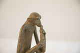 Close-up profile of a vintage monkey sculpture eating, showing its rustic patina.