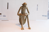 Handmade African sitting monkey sculpture showing the aged surface and slender limbs.