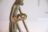 Vintage monkey sculpture's side view, showing aged texture on the torso and slender arms.